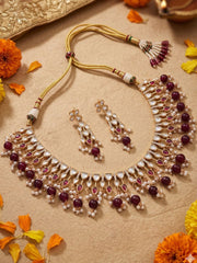 gold plated Ornate polki kundan necklace and earrings set with maroon and white stones on a beige background with flowers.